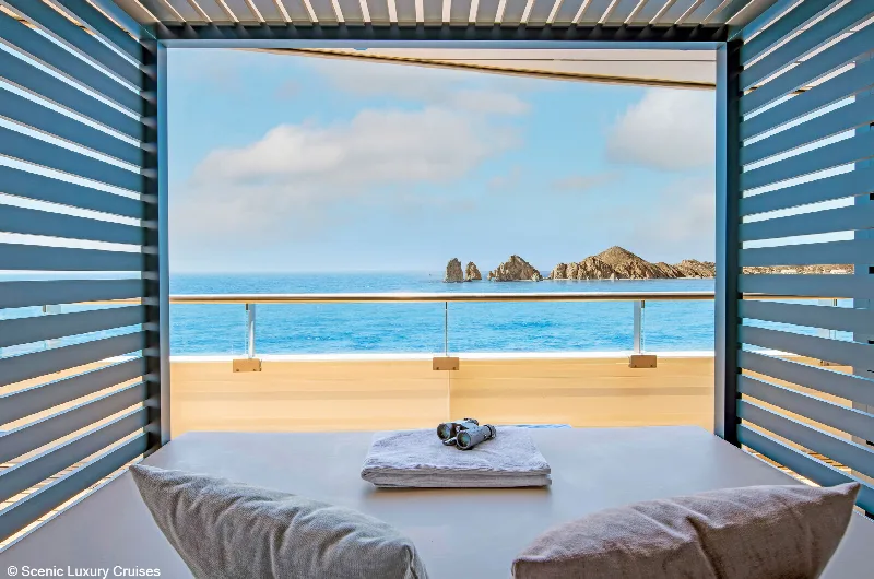Eine private Cabana an Deck mit Liegefläche, Handtuch und Sonnenbrille, dahinter das Meer und eine Felsküste