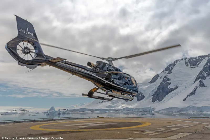 Ein Hubschrauber hebt vom Helideck eines Expeditionsschiffs vor den Bergen der Antarktis ab