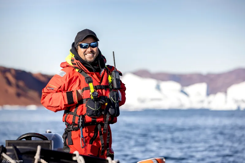 Ein Expeditionsguide in roter Jacke steht in einem Zodiac vor Eisbergen