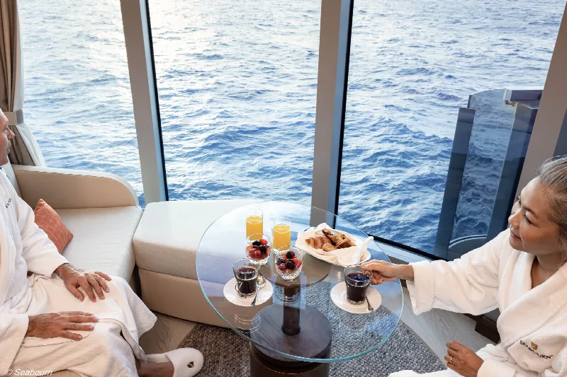 Zwei Gäste im Bademantel beim Frühstück am Panoramafenster einer Suite