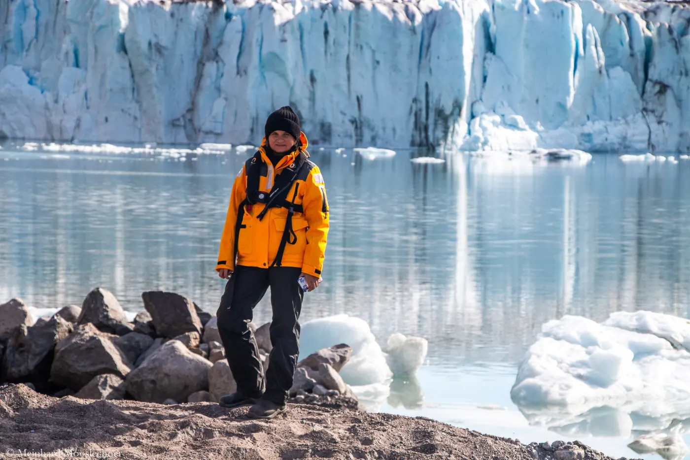 Daria Startseva in orangefarbener Expeditionsjacke vor einer Gletscherkante in Grönland