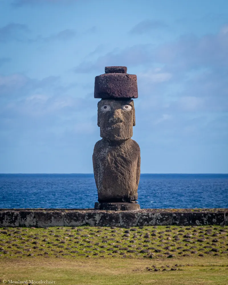 Ein Moai mit rotem Steinhut auf der Osterinsel, dahinter der Pazifik