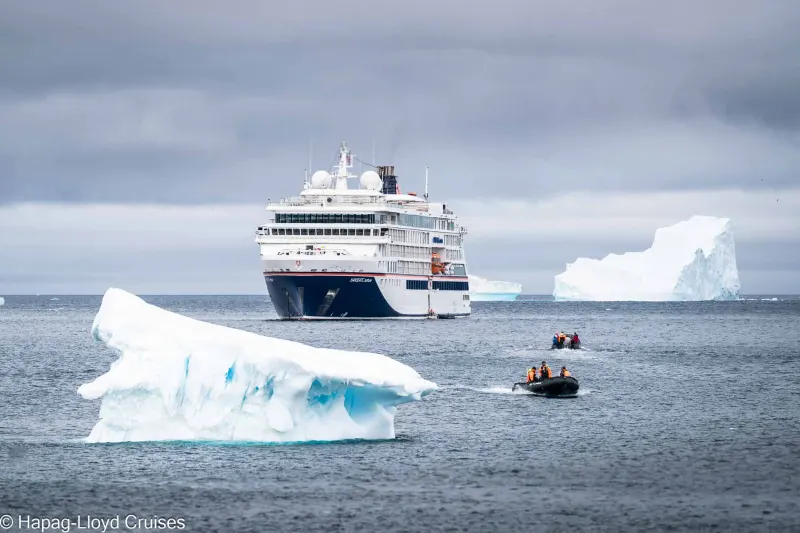 Das Expeditionsschiff Hanseatic nature von Hapag-Lloyd Cruises zwischen Eisbergen, davor zwei Zodiacs