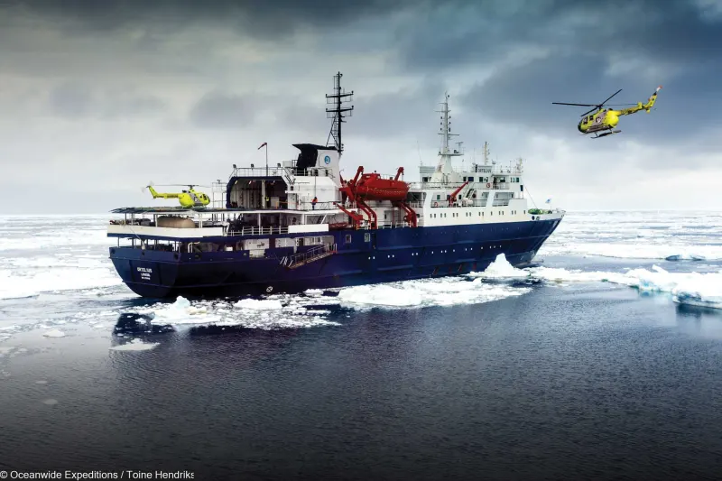 Das Expeditionsschiff Ortelius von Oceanwide Expeditions im Treibeis, ein Hubschrauber an Deck und einer in der Luft